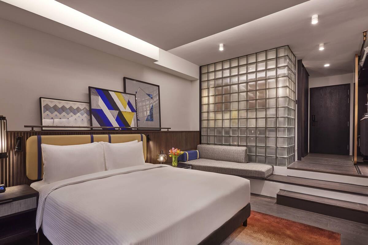 Una habitación de hotel moderna con una cama grande, un área de descanso y un muro decorativo.