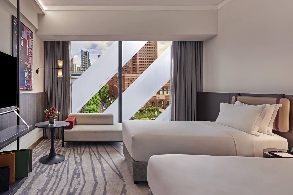 Habitación de hotel moderna con dos camas, un sofá, un televisor y vistas a la ciudad.