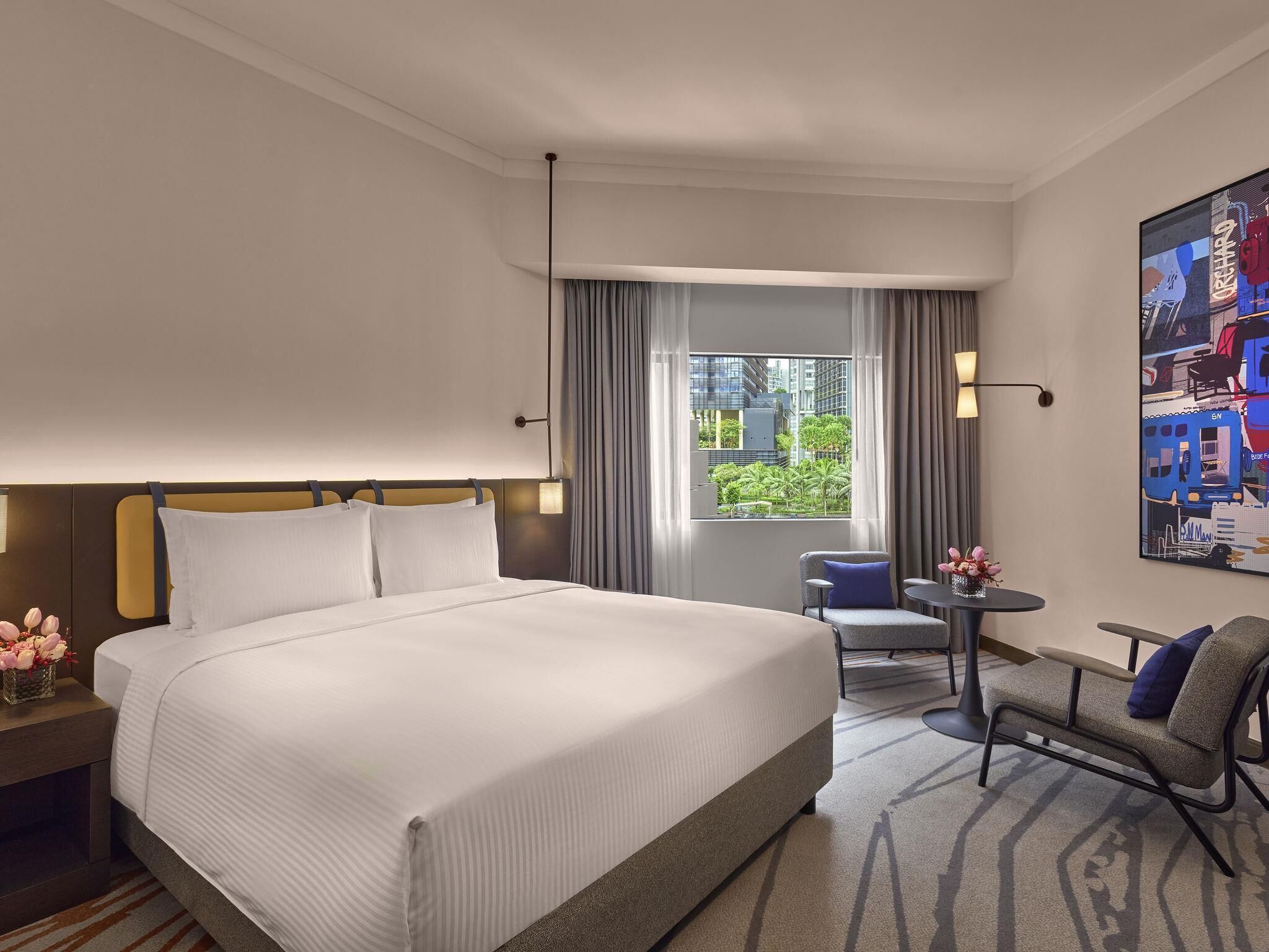 Ein Hotelzimmer mit einem großen Bett, einem Sessel, einem kleinen Tisch, einem Fenster mit Vorhängen und einem Wandbild.