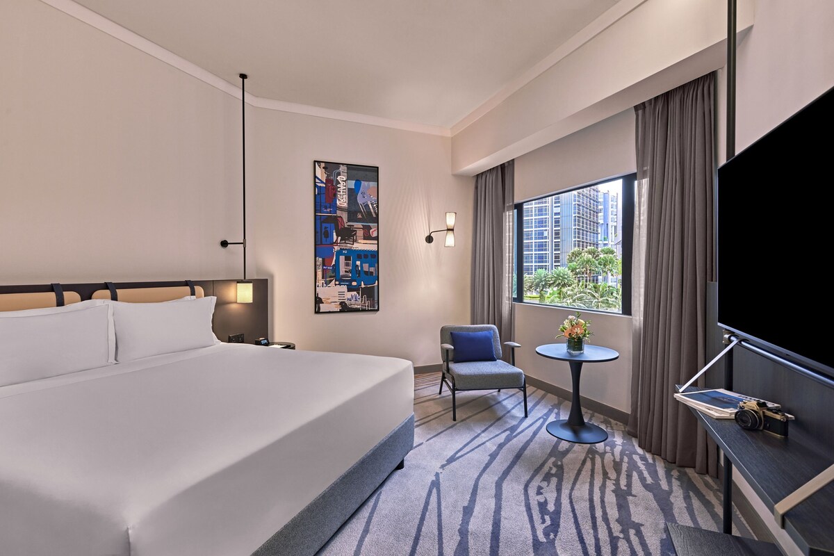 Habitación de hotel con una cama grande, una mesita con una silla, un televisor y un cuadro en la pared.