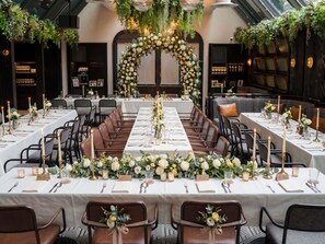 Een lange eettafel met witte tafelkleden, bruine lederen stoelen en bloemstukken.