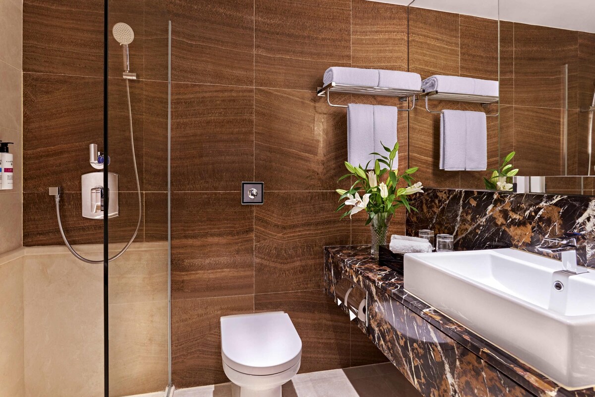 A modern bathroom with a marble vanity, a white toilet, a glass-enclosed shower, and a large mirror.