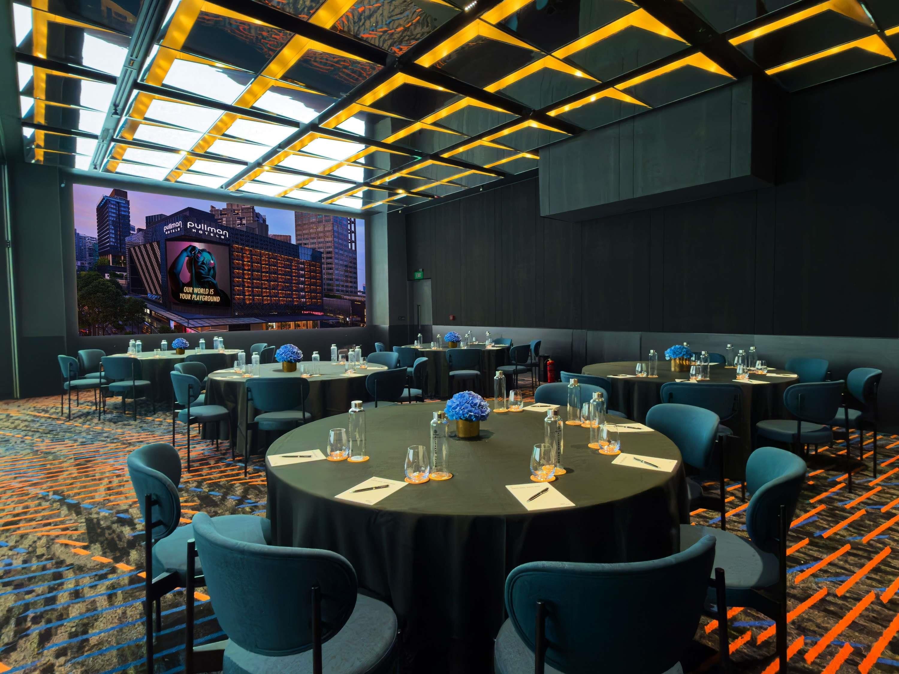 A conference room with tables set for meetings, a large screen displaying a cityscape, and a patterned carpet.