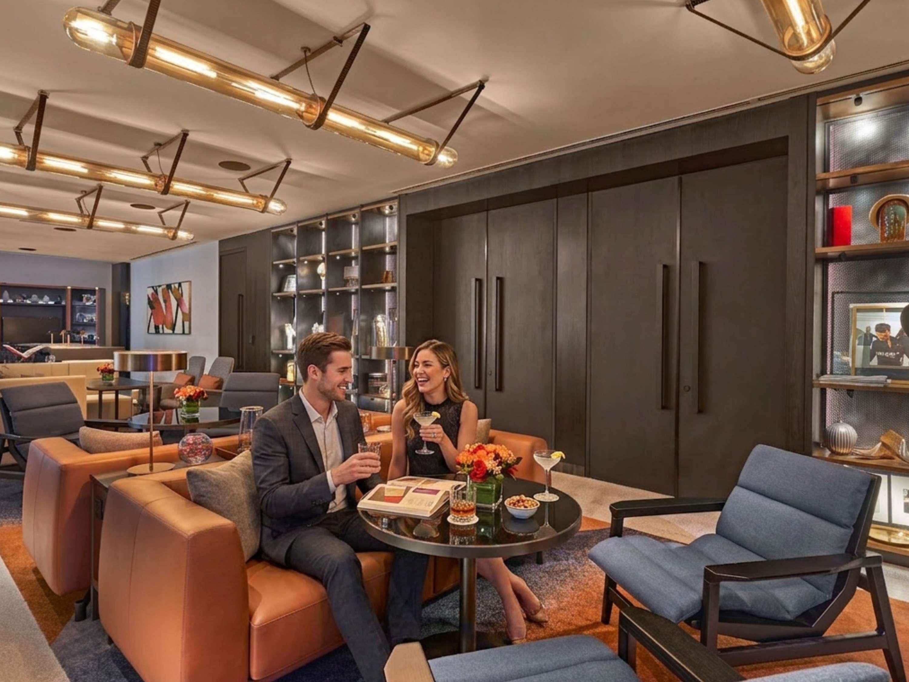 Un moderno vestíbulo de hotel con asientos de cuero, una mesa redonda con bebidas y una gran estantería.