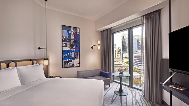 Habitación de hotel con una cama grande, un sofá, una mesita, un televisor y vistas a la ciudad por la ventana.