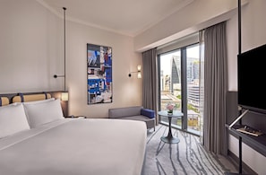 Hotelkamer met een groot bed, een bank, een klein tafeltje, een televisie en uitzicht op de stad.