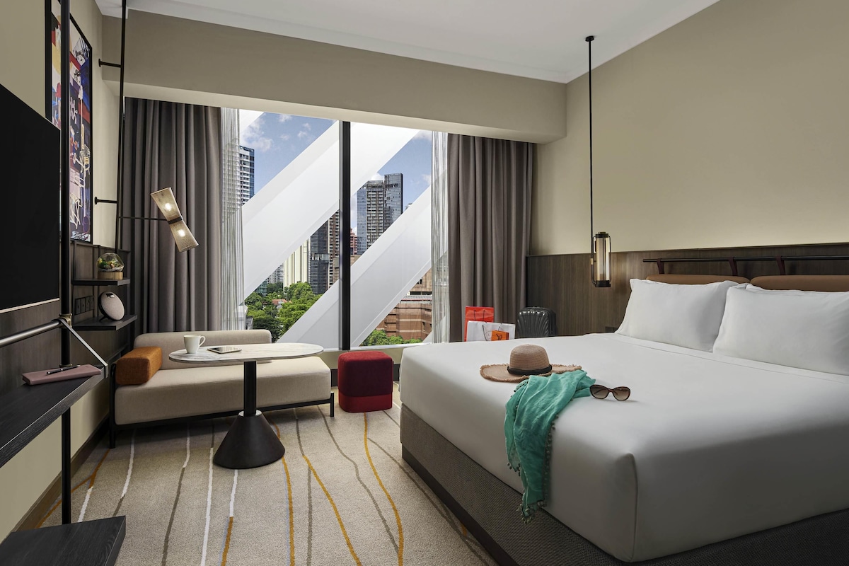 Habitación de hotel con cama, sofá, una mesita, televisor y vistas a la ciudad.
