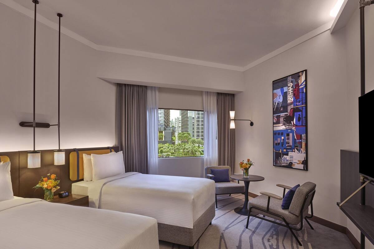 Habitación de hotel con dos camas, un escritorio, una silla, un televisor y un amplio ventanal con cortinas.