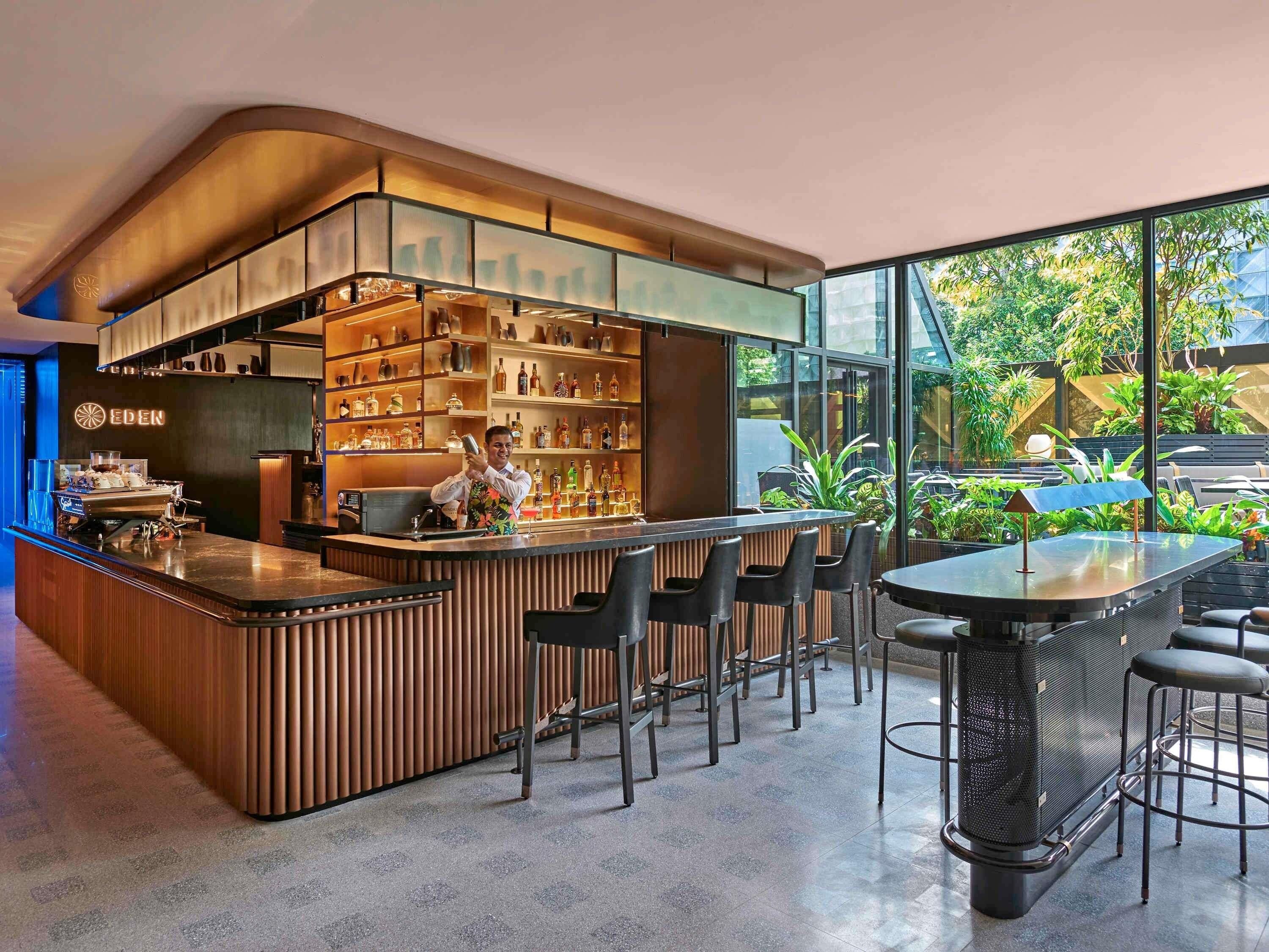 A modern bar area with a bartender, bar counter, seating, and shelves of bottles.