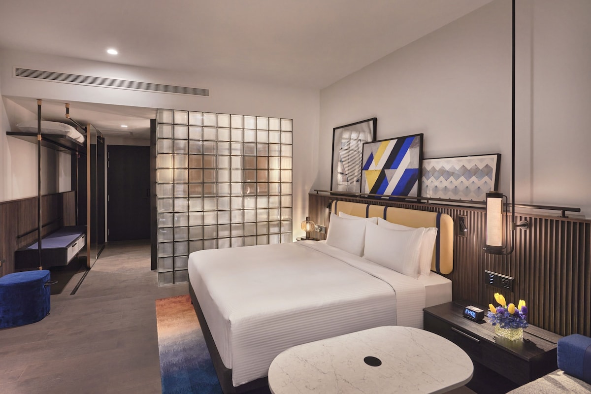 Una habitación de hotel moderna con una cama grande, un escritorio, una silla, una mesita y un televisor.