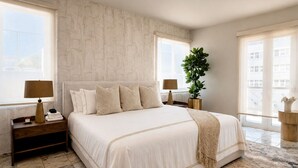 A bedroom with a large bed, two bedside tables, a nightstand, a potted plant, and a view of the outside.