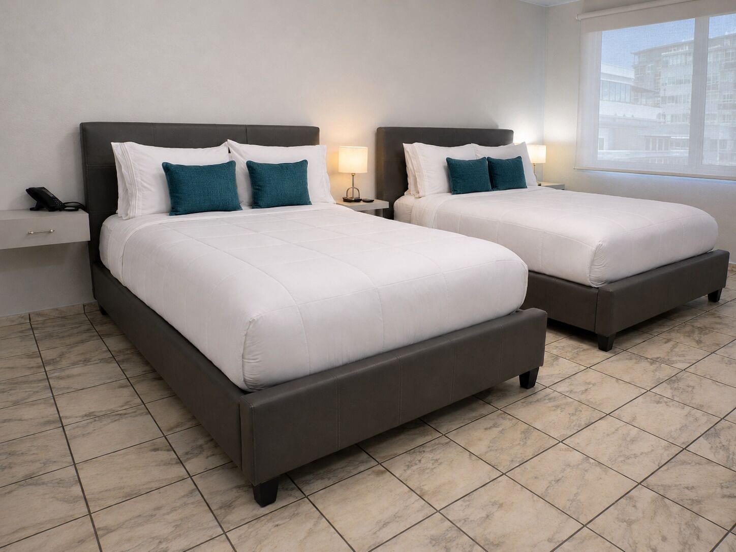 Habitación doble con dos camas, una mesita de noche, una lámpara y un teléfono a la izquierda.