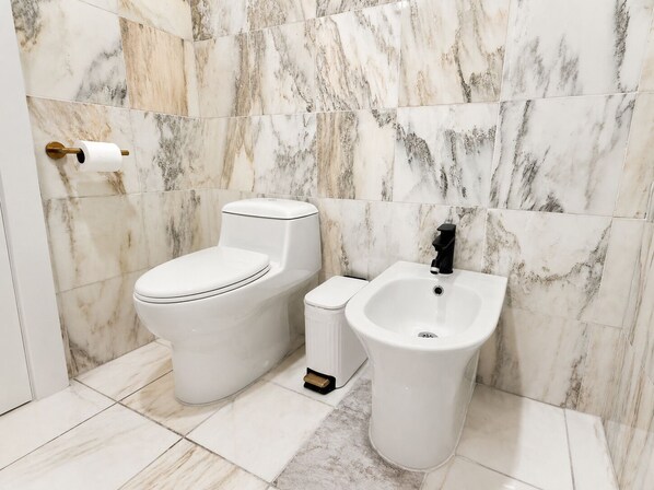 A bathroom with a toilet, bidet, and a marble wall.
