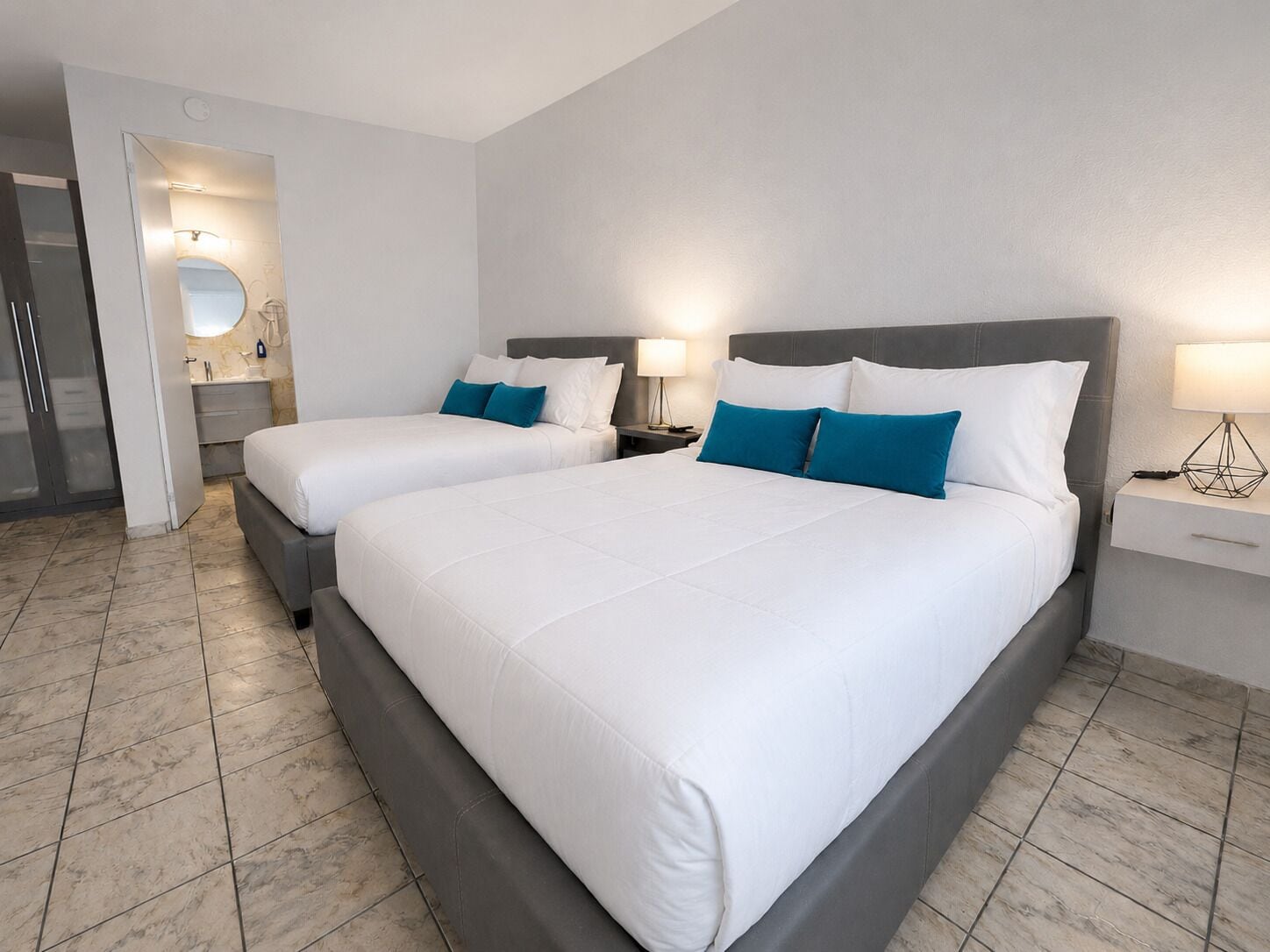 A hotel room with two beds, a bathroom, and a mirror.