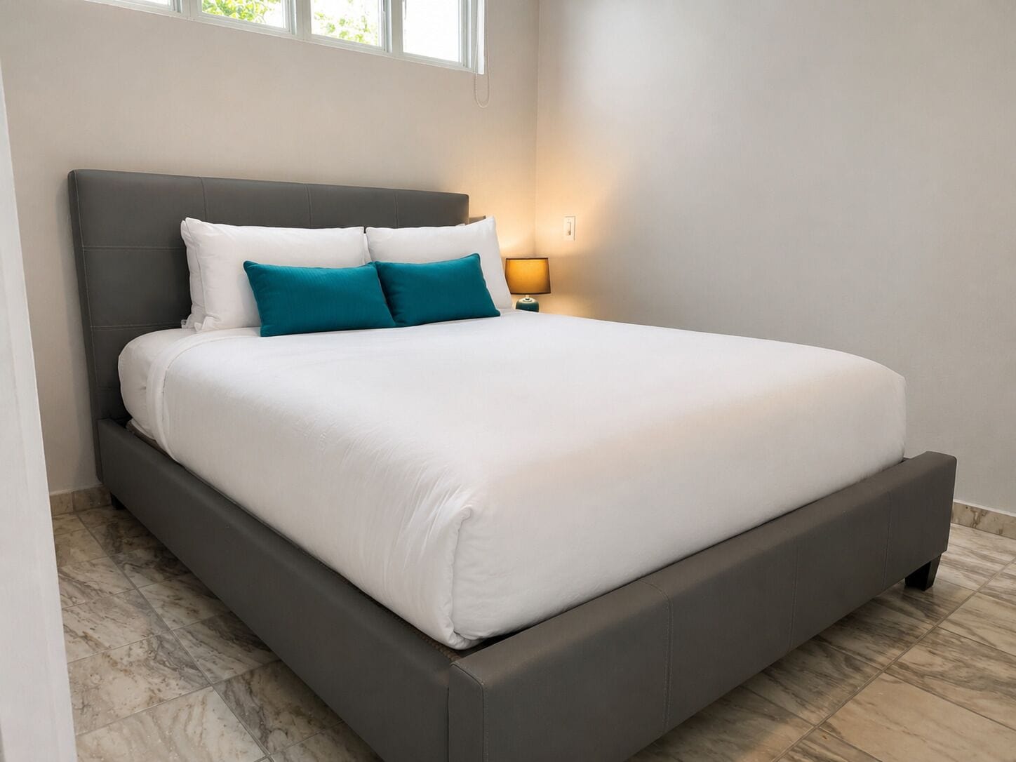A modern bedroom with a large bed, a nightstand, a lamp, and a window.