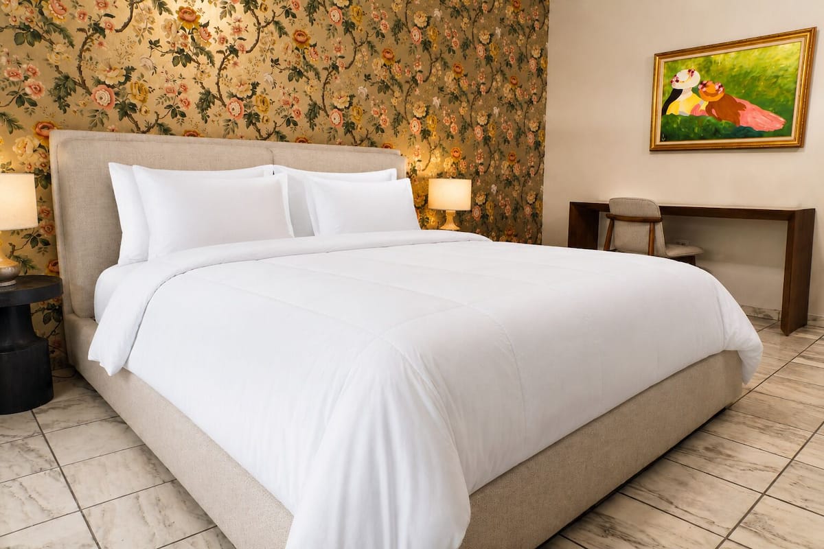 A neatly made bed with white linens, a headboard, and two bedside lamps.