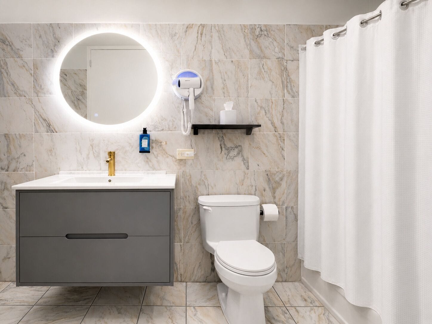 A bathroom with a marble-tiled wall, a round mirror, a white toilet, a grey vanity, and a shower curtain.