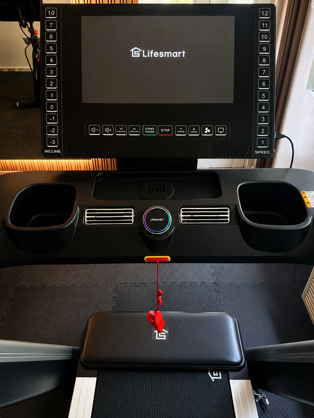 A treadmill with a digital display, control buttons, and a red cord.