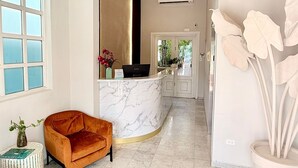 A modern interior with a marble reception desk, a plush orange sofa, and a large potted plant.
