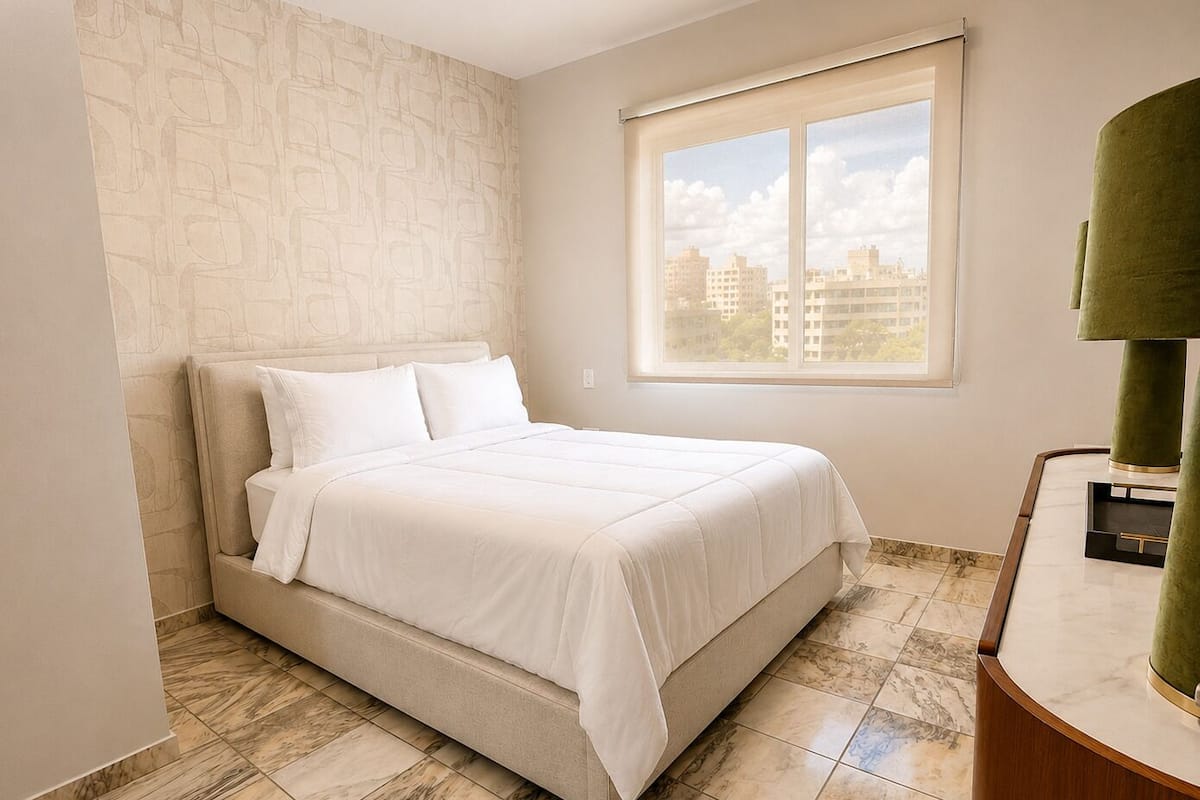A bedroom with a bed, a window with a city view, a marble floor, and a green lamp.
