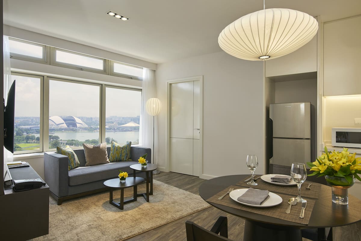 Ein modernes Wohnzimmer mit einer Couch, einem Couchtisch, einem Esstisch für zwei Personen und einem großen Fenster mit Blick auf die Stadt.