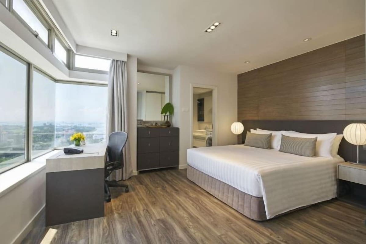 Habitación de hotel moderna con una cama grande, un escritorio con silla, una cómoda y vistas a la ciudad.