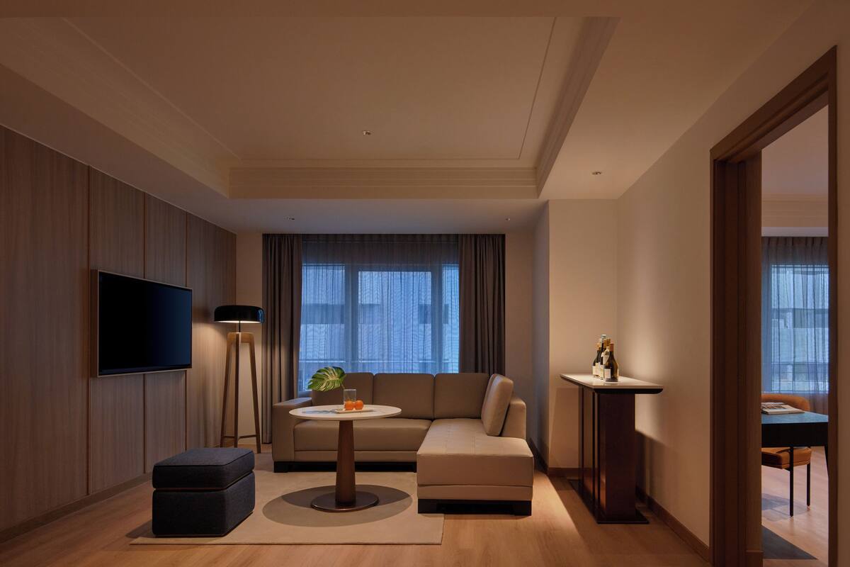 A modern living room with a flat-screen TV, a round coffee table, a sofa, and a small side table with bottles.