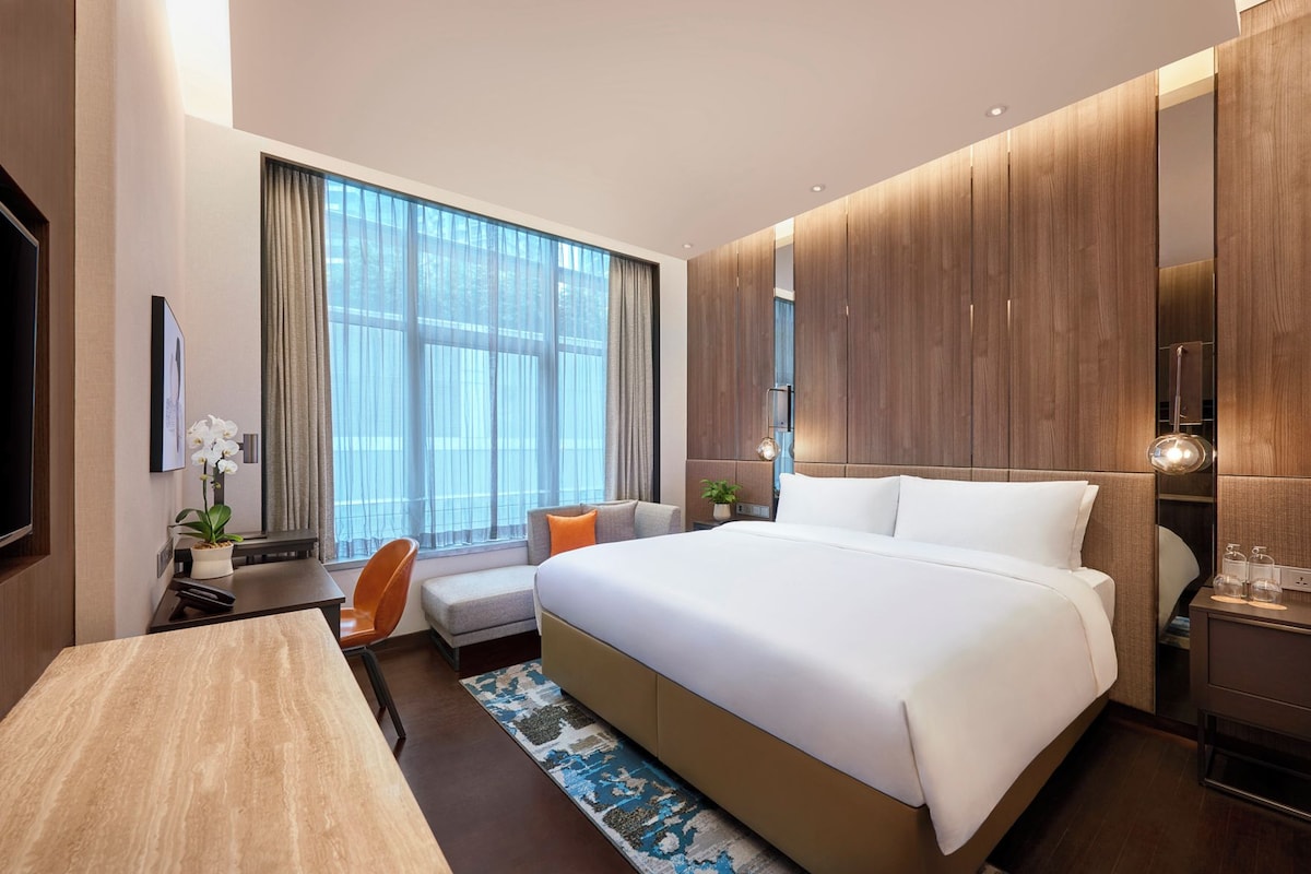 A modern hotel room with a large bed, a desk, a chair, and a television.