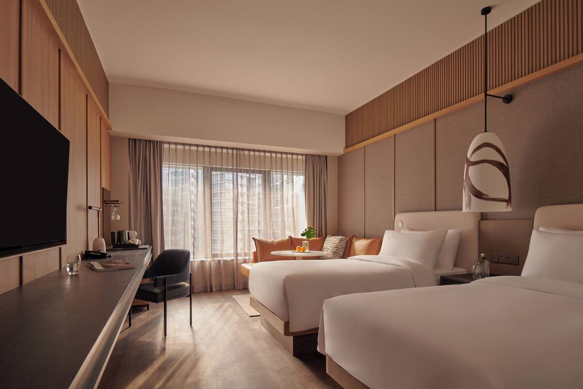 A modern hotel room with a large bed, a desk with a flat-screen TV, a sofa, and a dining table.