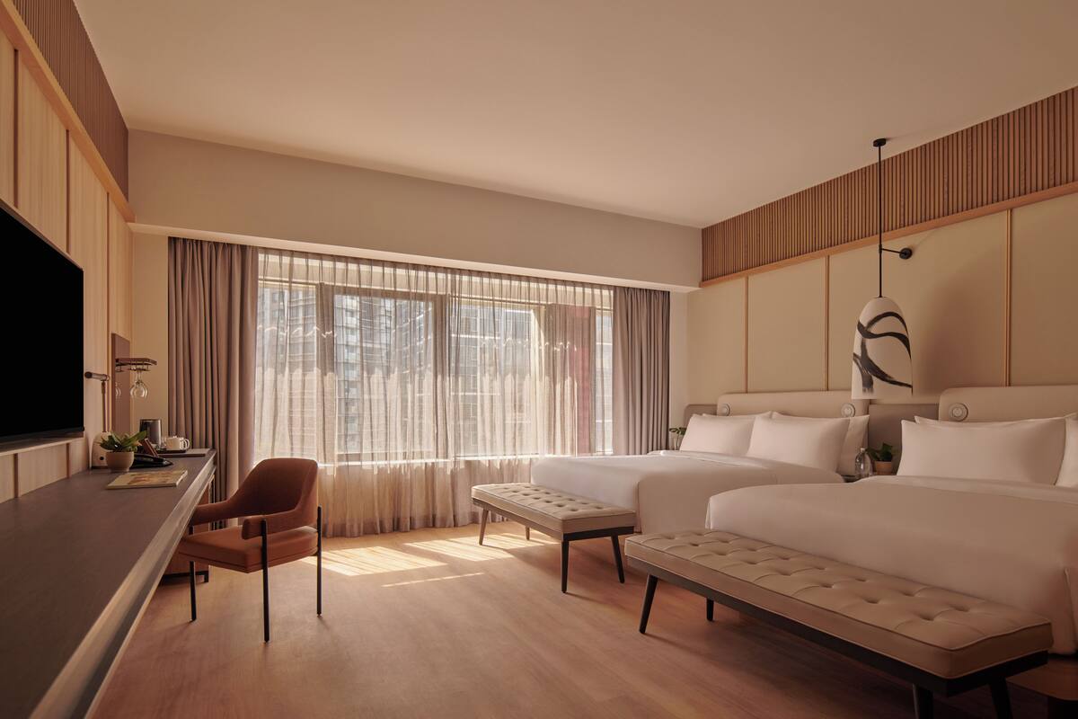 A hotel room with a large bed, a smaller bed, a desk with a chair, and a large window with curtains.