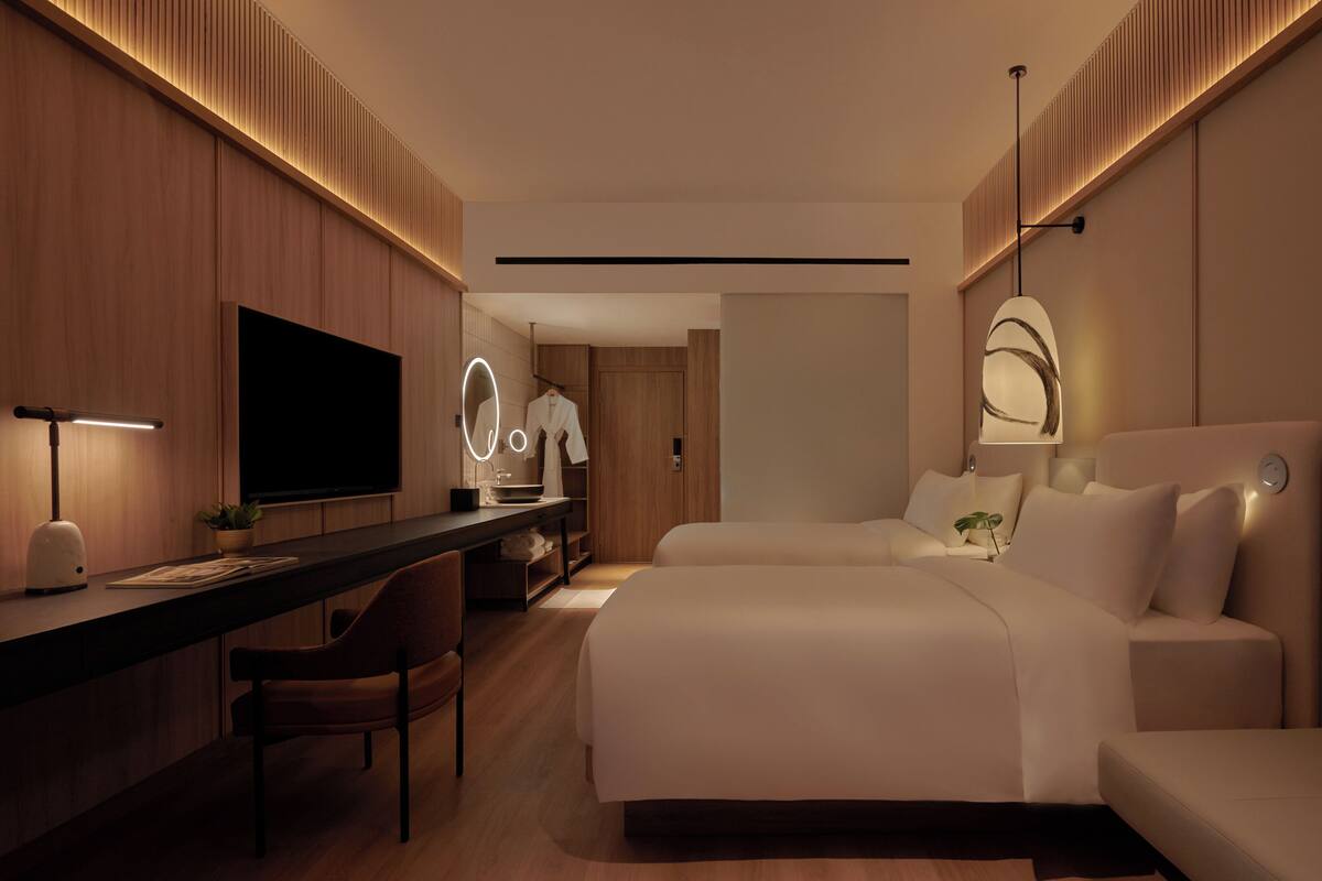 A modern hotel room with a large bed, a desk with a flat-screen TV, a vanity with a mirror, and a sofa.