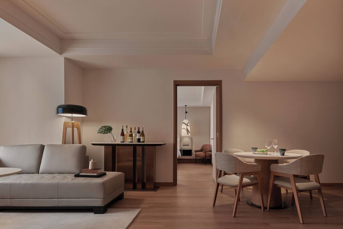 A modern living room with a sofa, a dining table with chairs, a lamp, and a fireplace.