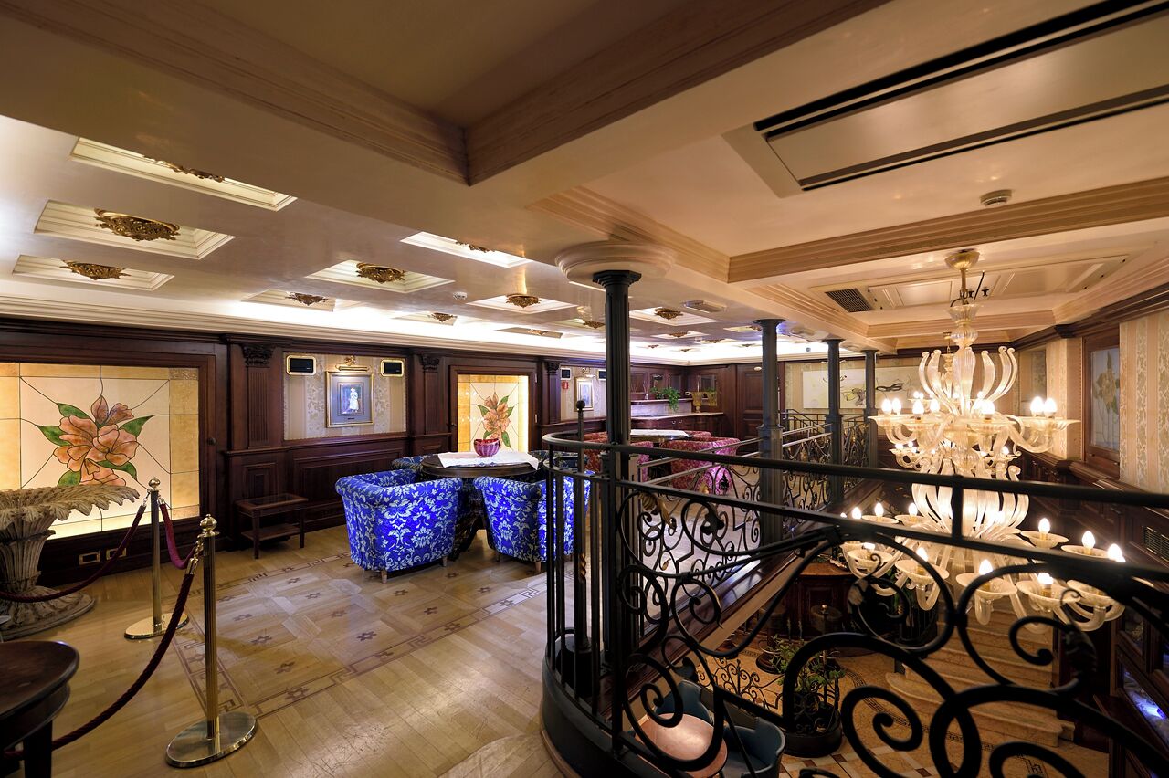 A grand lobby with a wooden floor, a staircase with ornate railings, and a chandelier.