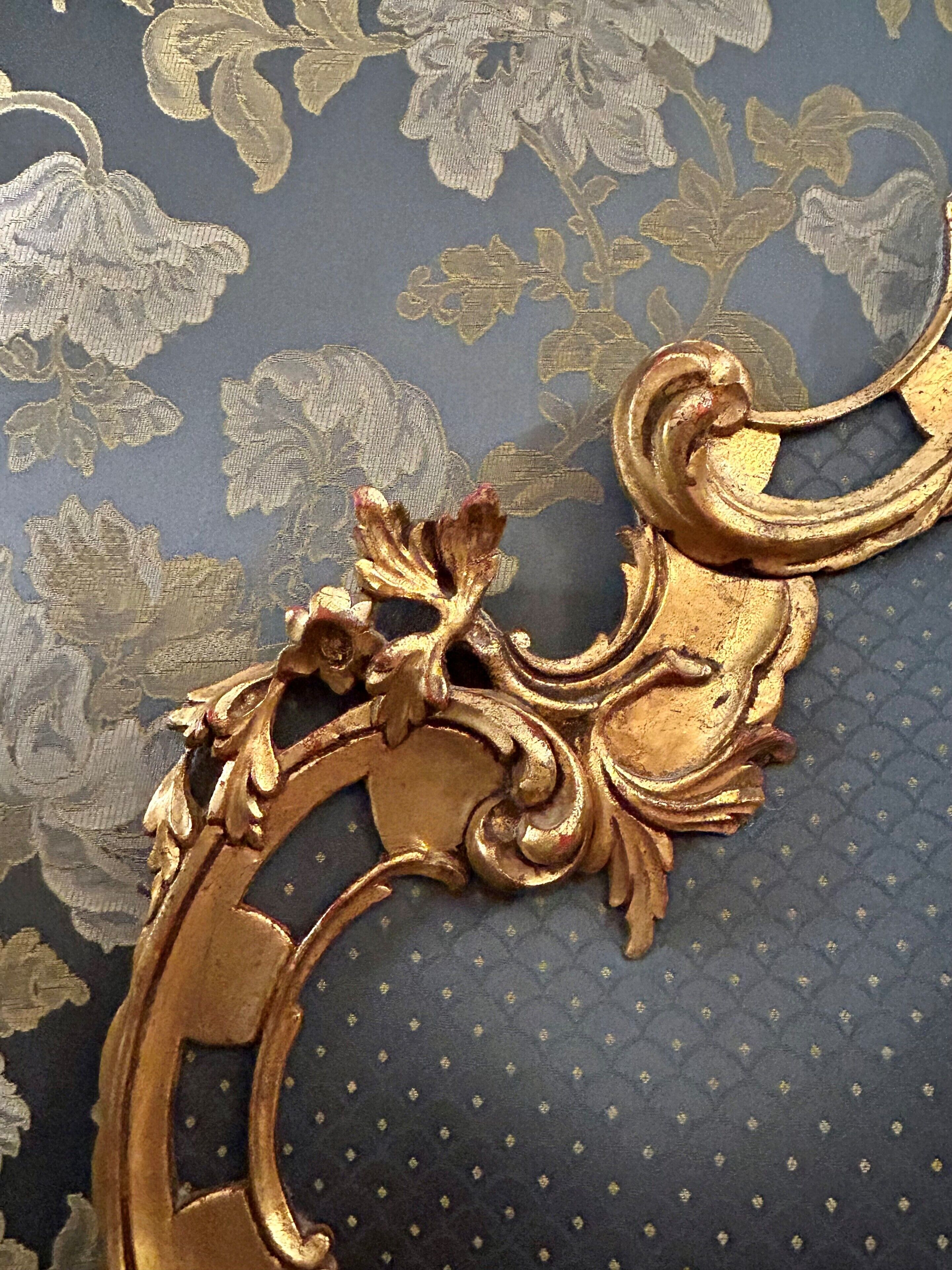 A close-up of a golden ornate metalwork piece with floral patterns, set against a dark blue fabric with a subtle floral design.