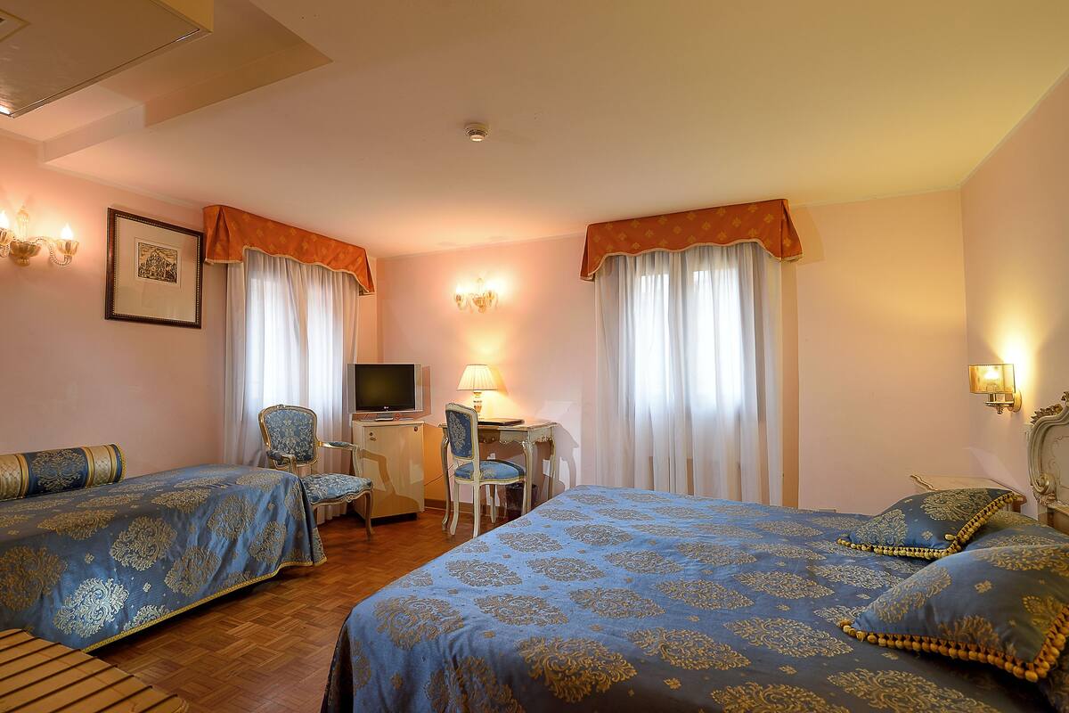 A hotel room with two beds, a desk, a chair, and a television.