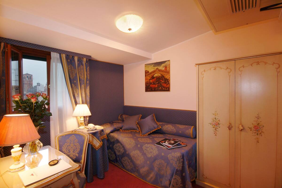 A hotel room with a bed, bedside table, lamp, and a wardrobe.