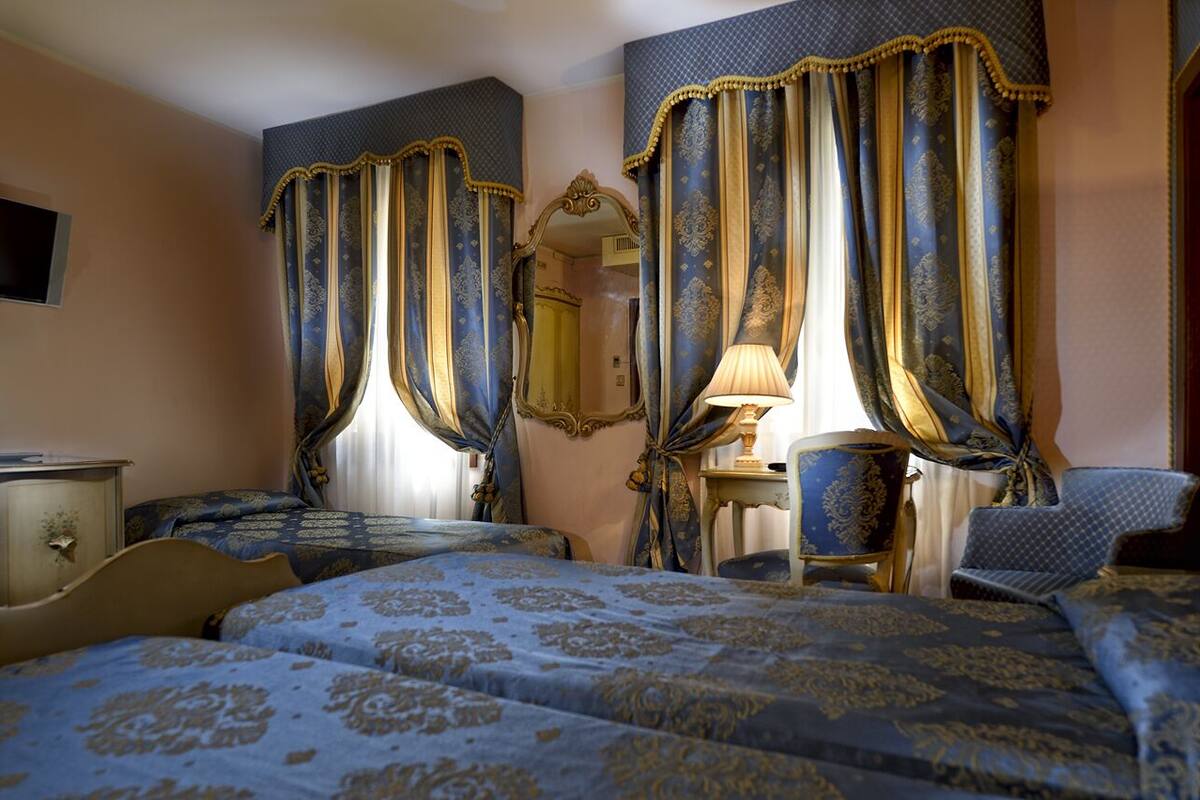 A hotel room with two beds, a sitting area with a chair, a lamp, and a mirror.