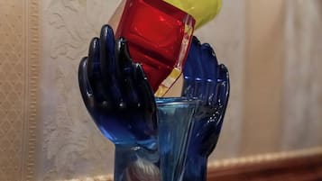 Una escultura de cristal decorativa que muestra manos sosteniendo una copa y un objeto rojo, sobre una superficie de madera.