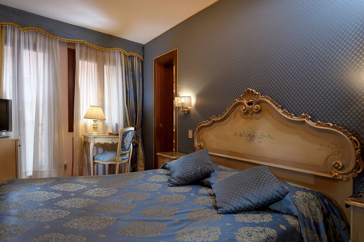 A hotel room with a large bed, a desk with a lamp, and a chair.