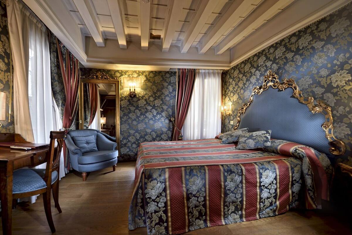 A bedroom with a large bed, a chair, a desk, and a mirror.