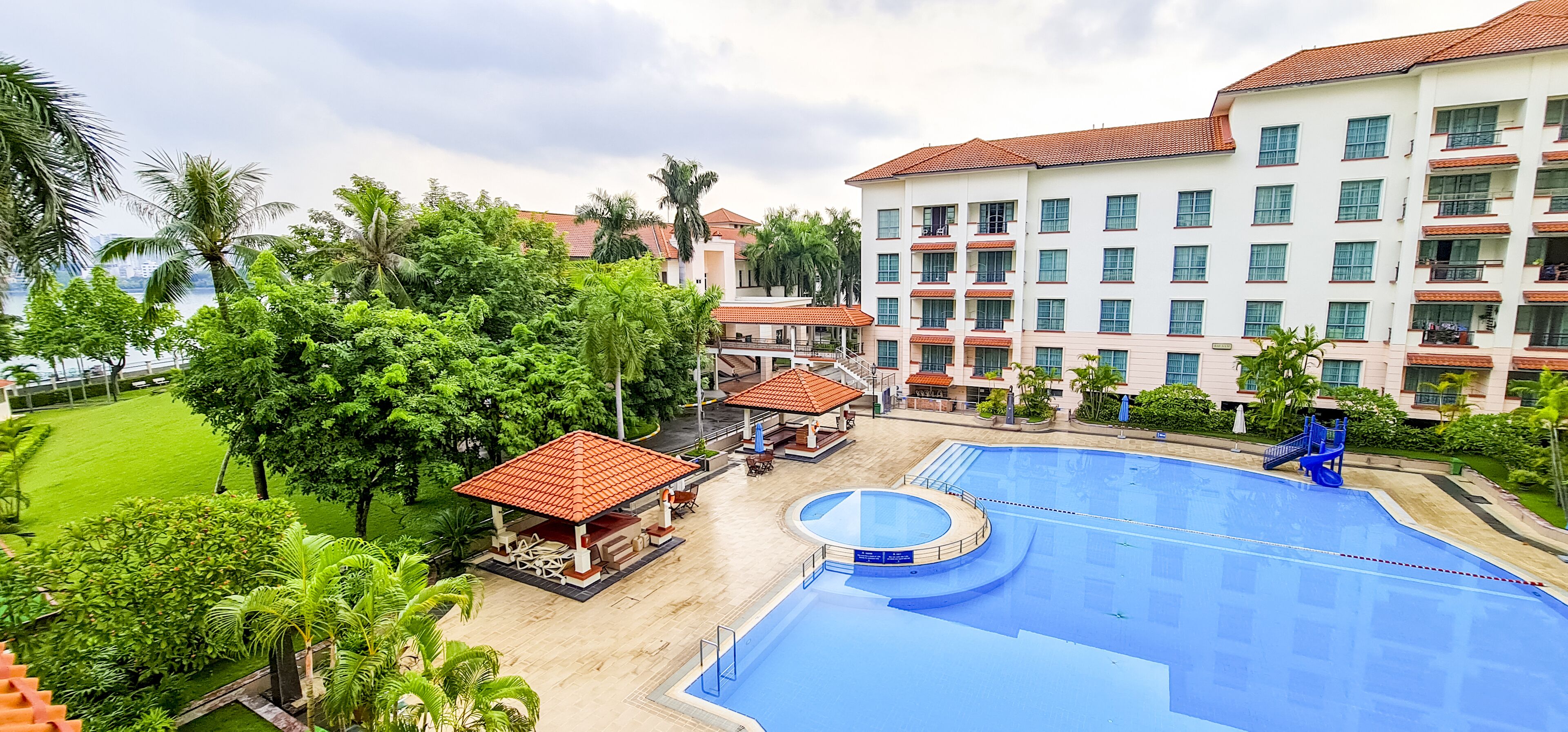 A hotel with a large swimming pool, palm trees, and a building with multiple balconies.