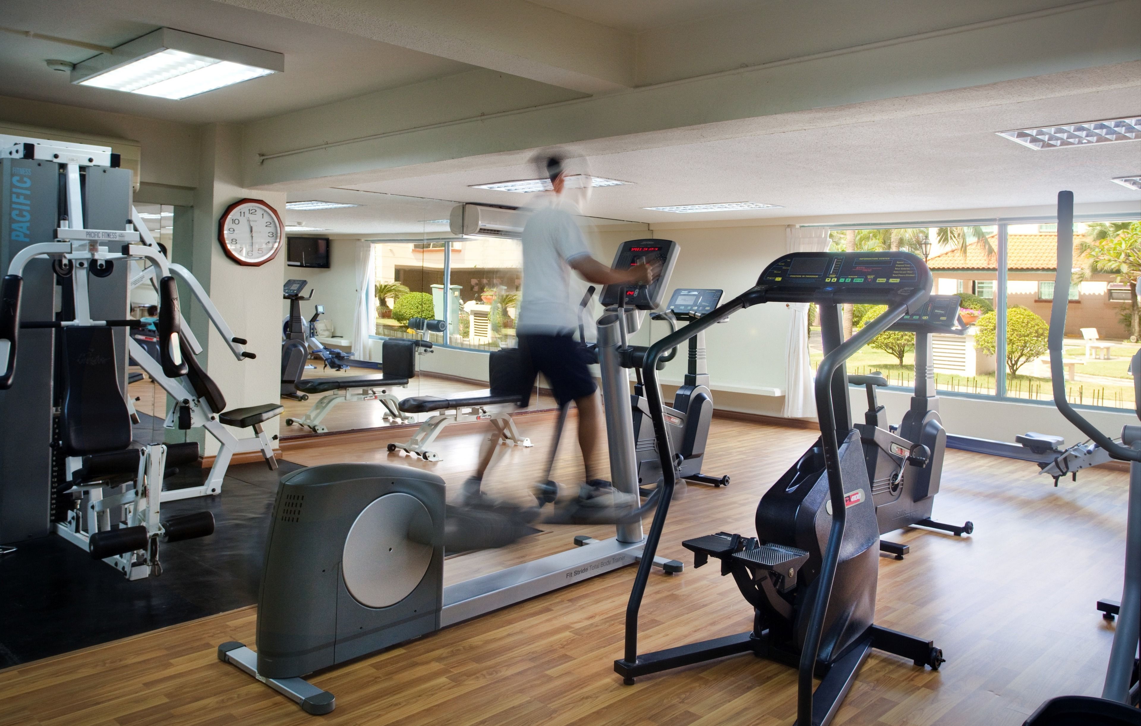 Una palestra con diverse attrezzature per l'allenamento, un orologio a parete e ampie finestre.