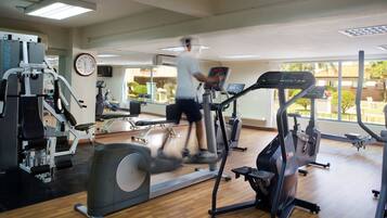 Una palestra con diverse attrezzature per l'allenamento, un orologio a parete e ampie finestre.