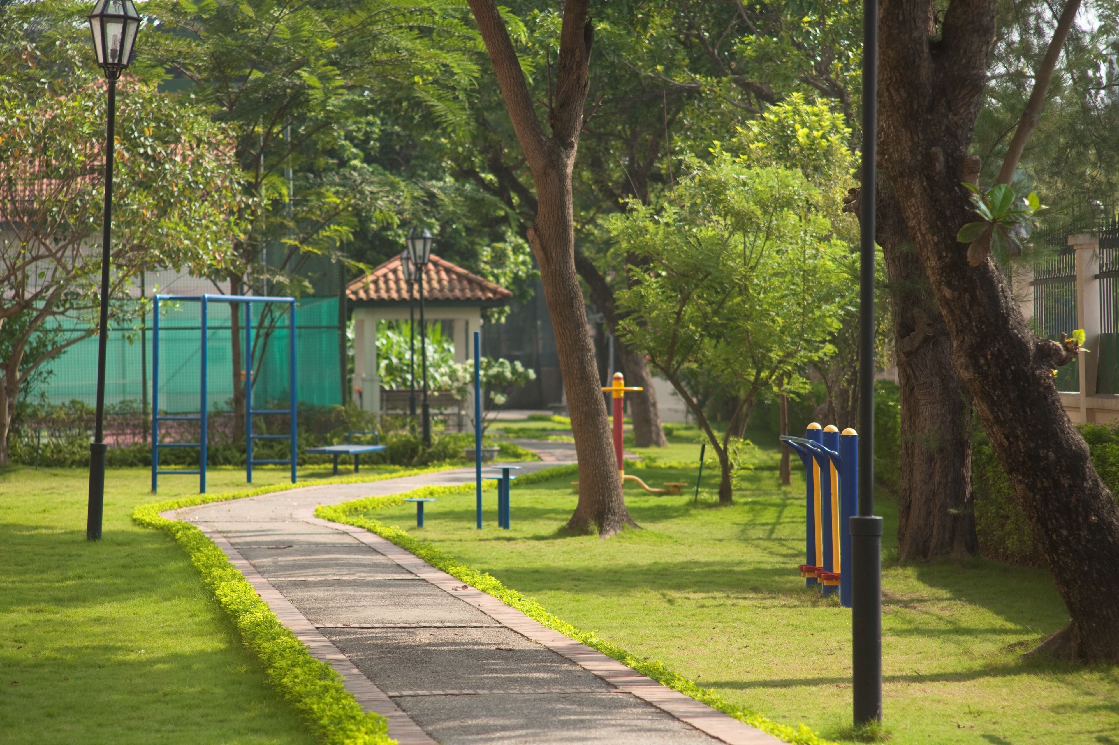 Un sendero en un parque con equipamiento para hacer ejercicio, bancos y un pabellón.