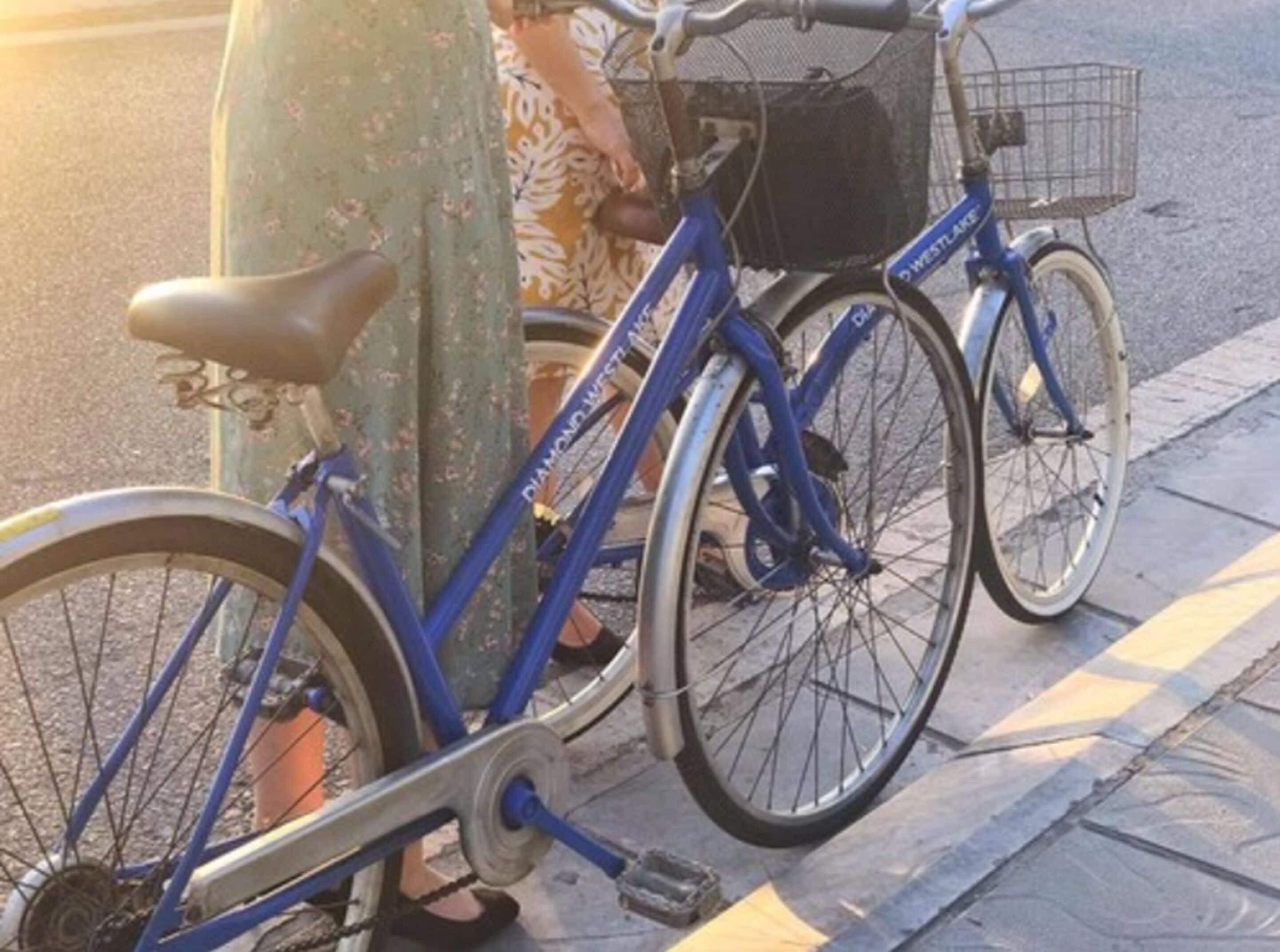 Een blauw fiets met een mandje, geparkeerd op een trottoir.