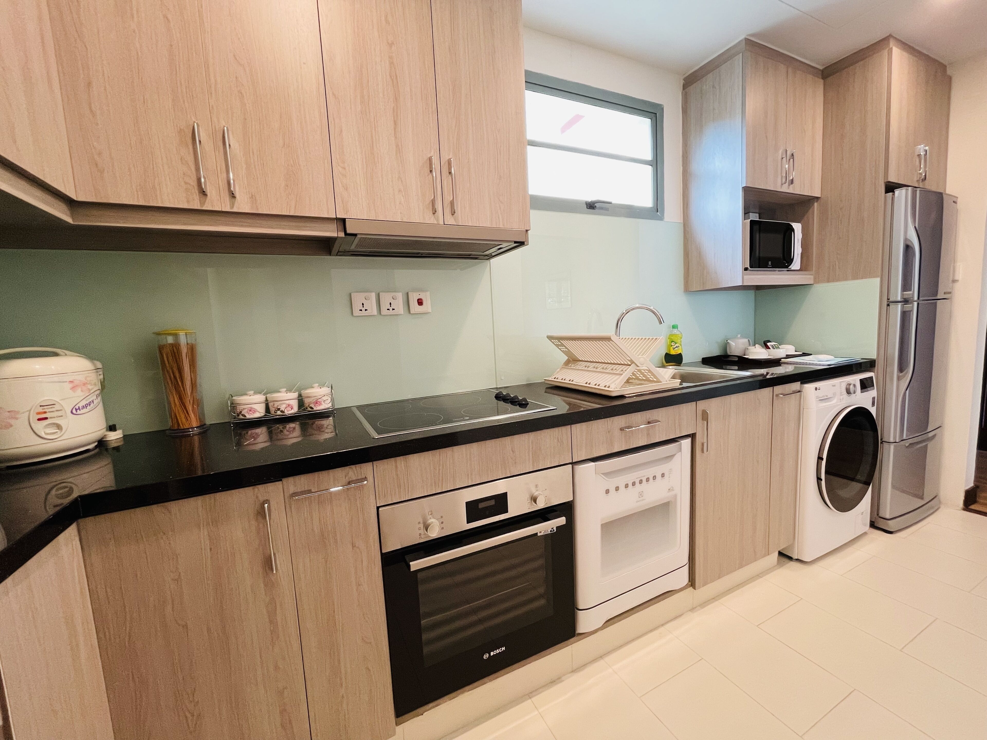 Une cuisine moderne avec des meubles en bois, un plan de travail noir, un four Bosch, un lave-linge et un four à micro-ondes.