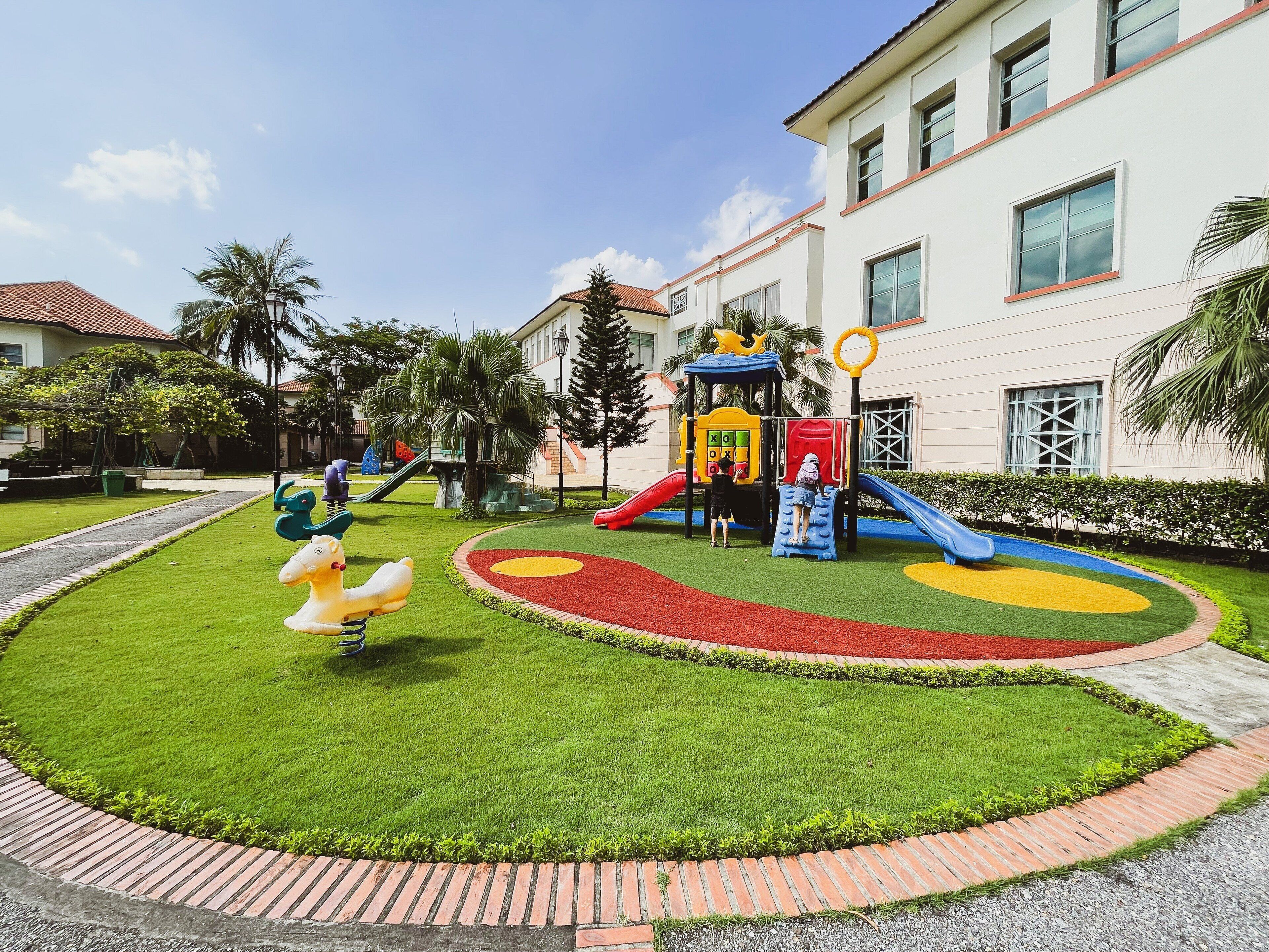 A playground with slides and climbing structures, surrounded by well-maintained grass and a brick pathway.