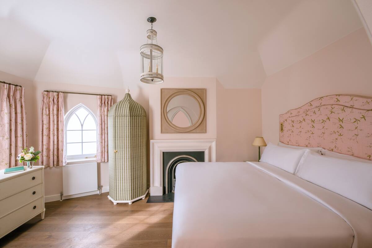 Een slaapkamer met een groot bed, een kaptafel, een raam met gordijnen, een spiegel en een open haard.