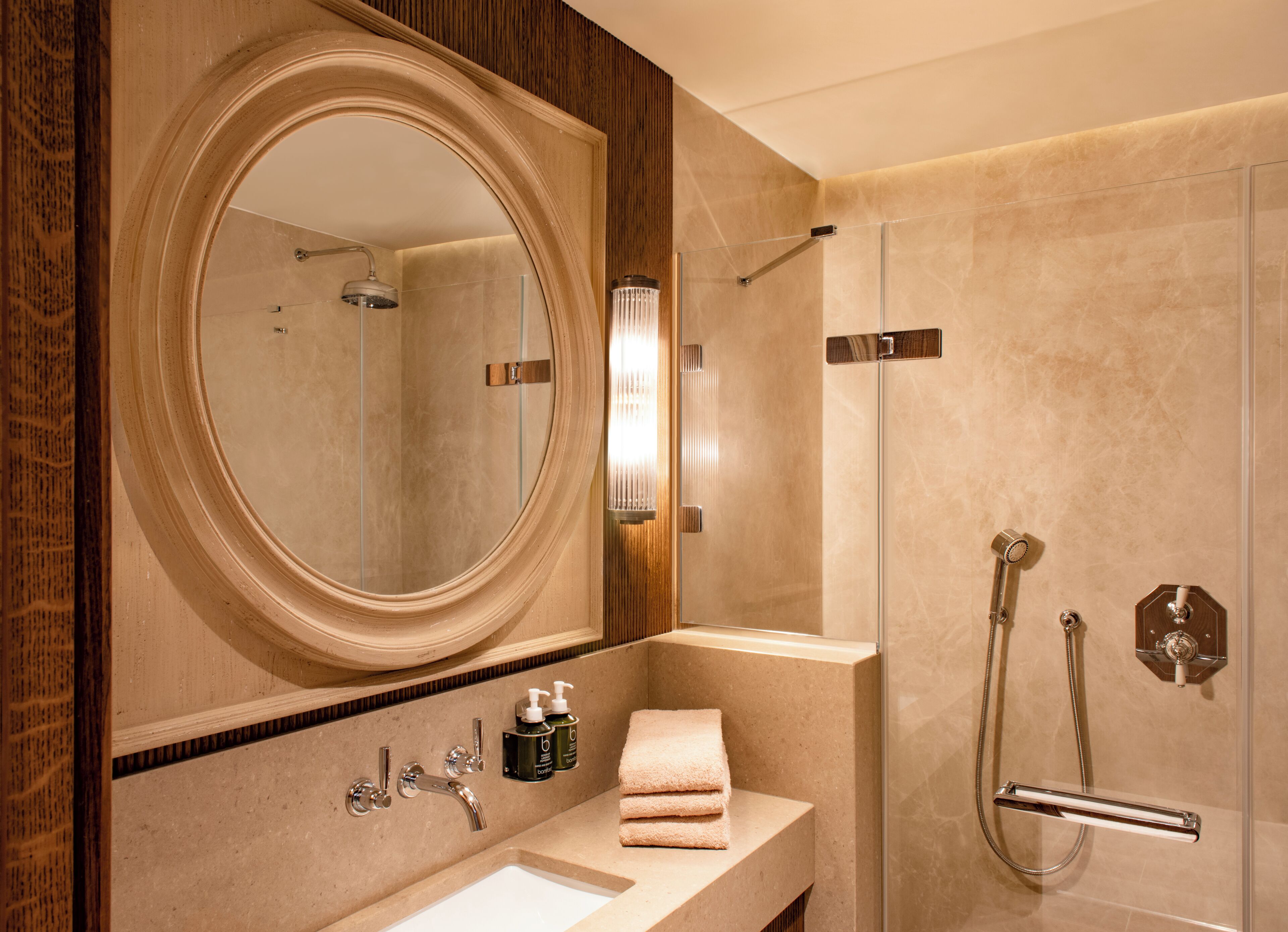 A modern bathroom with a large mirror, a glass-enclosed shower, a sink, and toiletries.