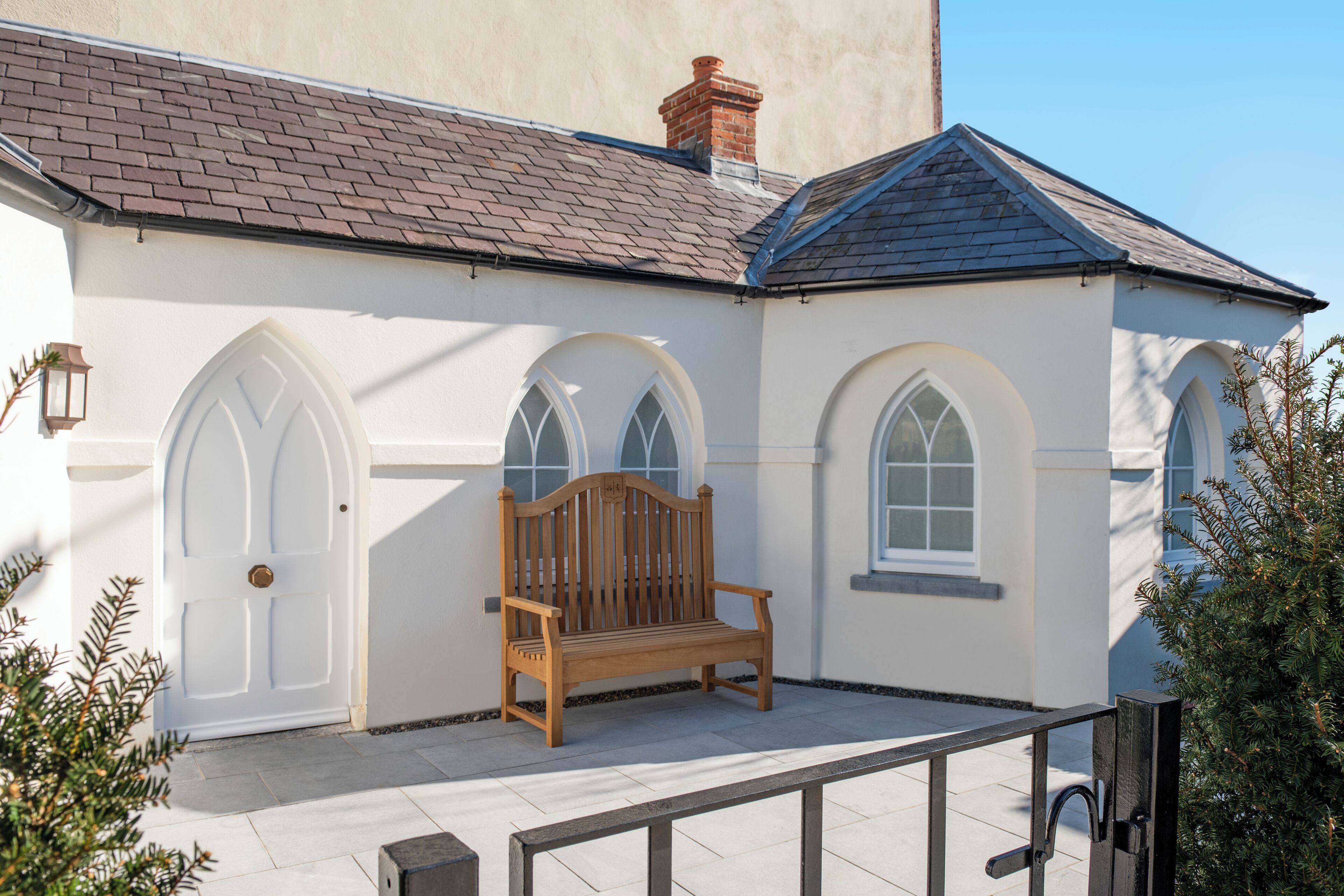 A white building with a wooden bench, arched windows, and a tiled roof.